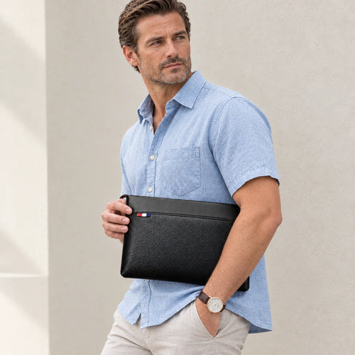 Homme en chemise bleue tenant la pochette noire sous le bras